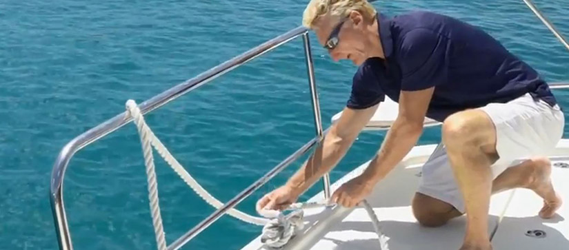 man bending down on a boat tying a rope to a cleat